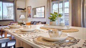 A dining area with a long table set for four, featuring woven placemats and a central plant. - Bozeman/4Corners HomeBase • River Access & Fire Pit • Close to Skiing and Hiking (Bozeman)