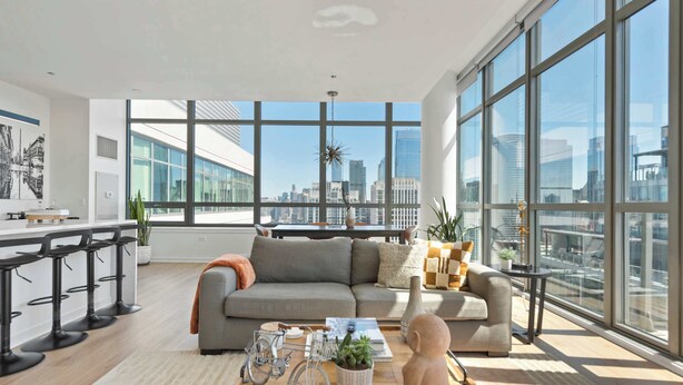 A modern living room with a large window, a grey sofa, a coffee table with a plant, and a city view. - Penthouse Escape + Vibrant West Loop Access (Chicago)