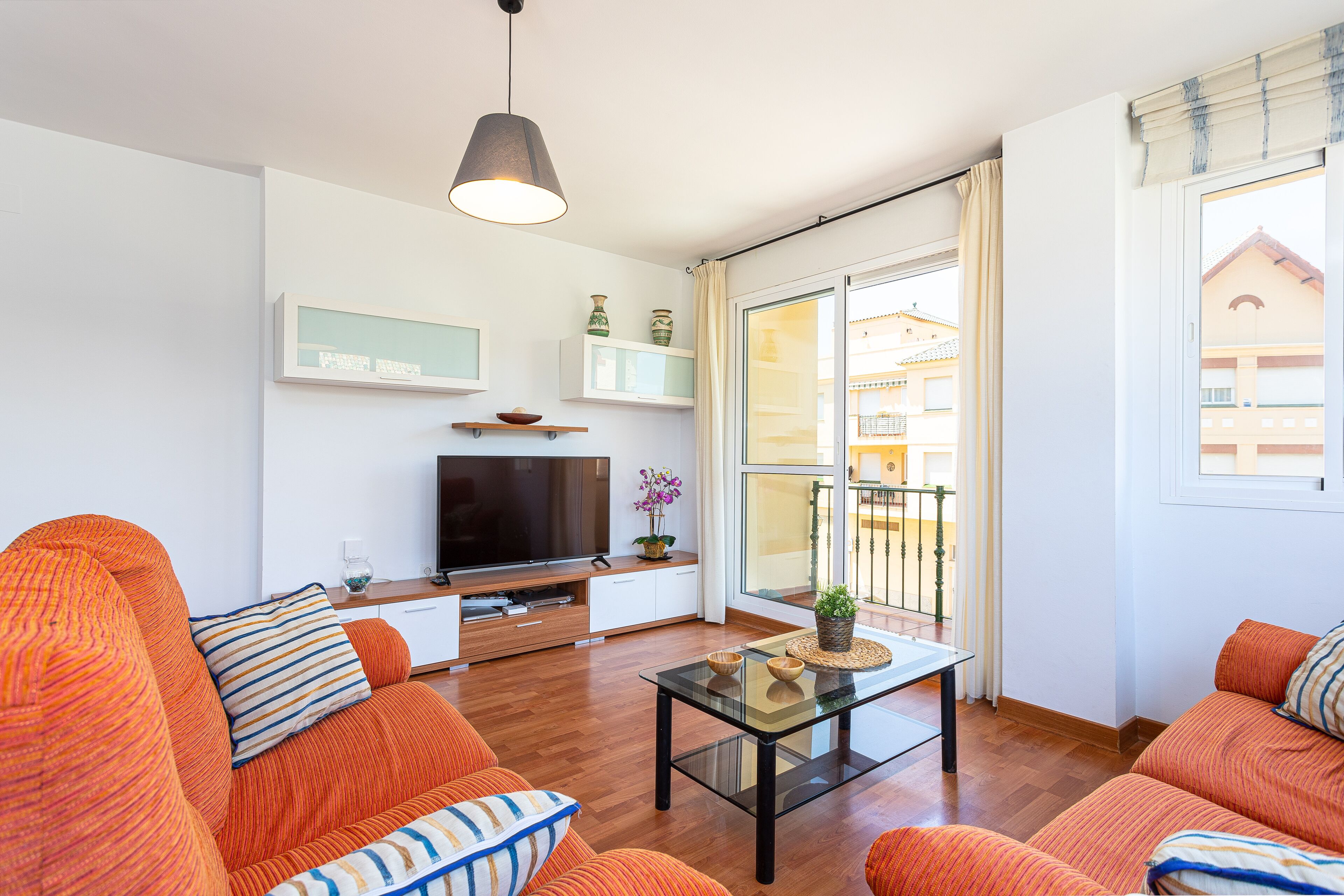 Een moderne woonkamer met oranje banken, een glazen salontafel, een flatscreen televisie en een balkon met uitzicht.