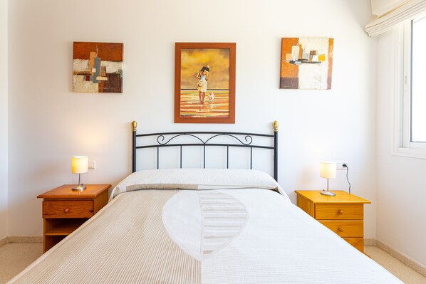 Une chambre à coucher avec un lit, deux tables de chevet et trois tableaux accrochés au mur.