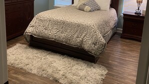 A bedroom with a bed, wooden dresser, ceiling fan, and decorative wall art. - Brick home in a quiet quaint neighborhood. Just minutes off the beach express. (Foley)