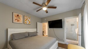 Un dormitorio con cama, ventilador de techo, televisor montado en la pared y zona de ducha.