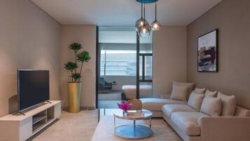 A modern living room with a flat-screen TV, a round coffee table, a sofa, a large potted plant, and a painting on the wall.