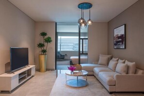 A modern living room with a flat-screen TV, a round coffee table, a sofa, a large potted plant, and a painting on the wall. - Steigenberger Hotel Doha (Doha)