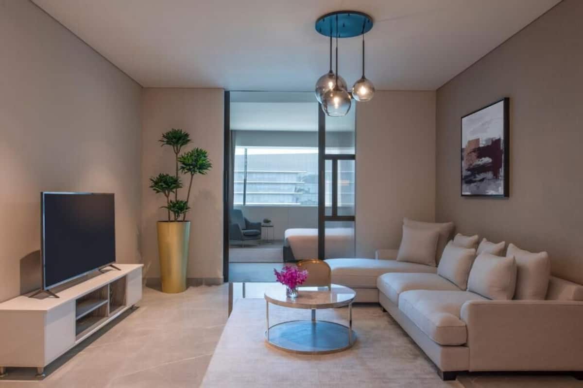 Una sala de estar moderna con un televisor de pantalla plana, una mesa de centro redonda, un sofá, una planta grande en maceta y un cuadro en la pared.