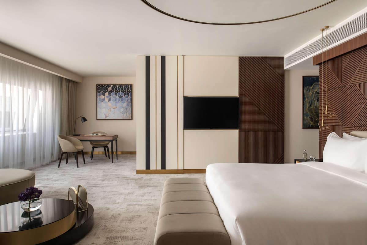Habitación de hotel moderna con una cama grande, un escritorio con sillas, un televisor de pantalla plana y obras de arte en las paredes.