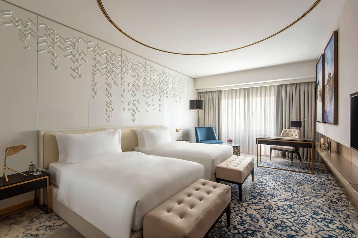 Habitación de hotel con dos camas, un escritorio, una silla, una mesita y alfombra estampada.