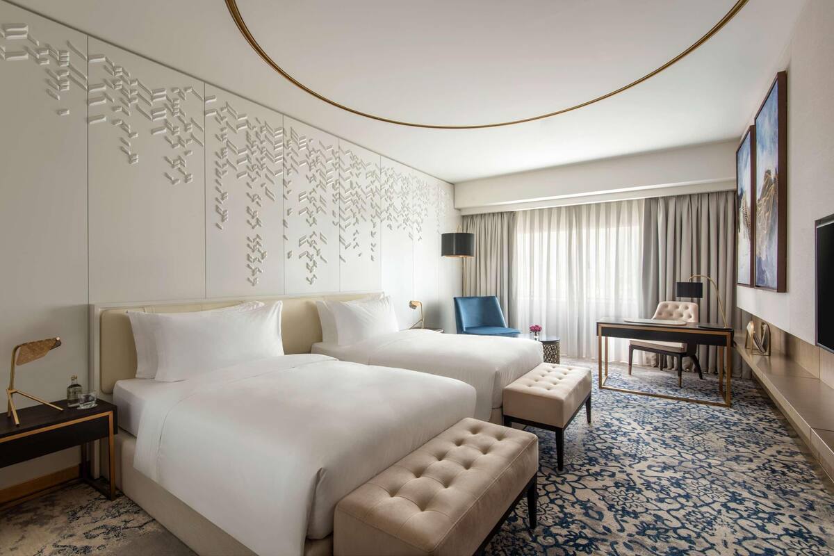 A hotel room with two beds, a desk, a chair, a small table, and a patterned carpet.