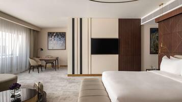 A modern hotel room with a large bed, a desk with chairs, a flat-screen TV, and artwork on the walls.