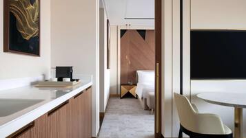 A modern hotel room with a kitchen area, a dining table, and a bed.