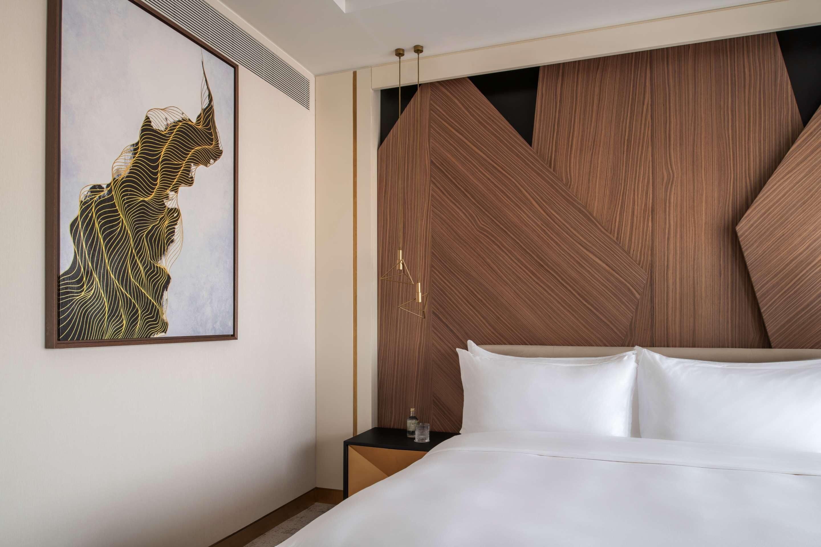 A modern hotel room with a large bed, a wooden accent wall, and a framed artwork on the wall.