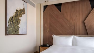 A modern hotel room with a large bed, a wooden accent wall, and a framed artwork on the wall.