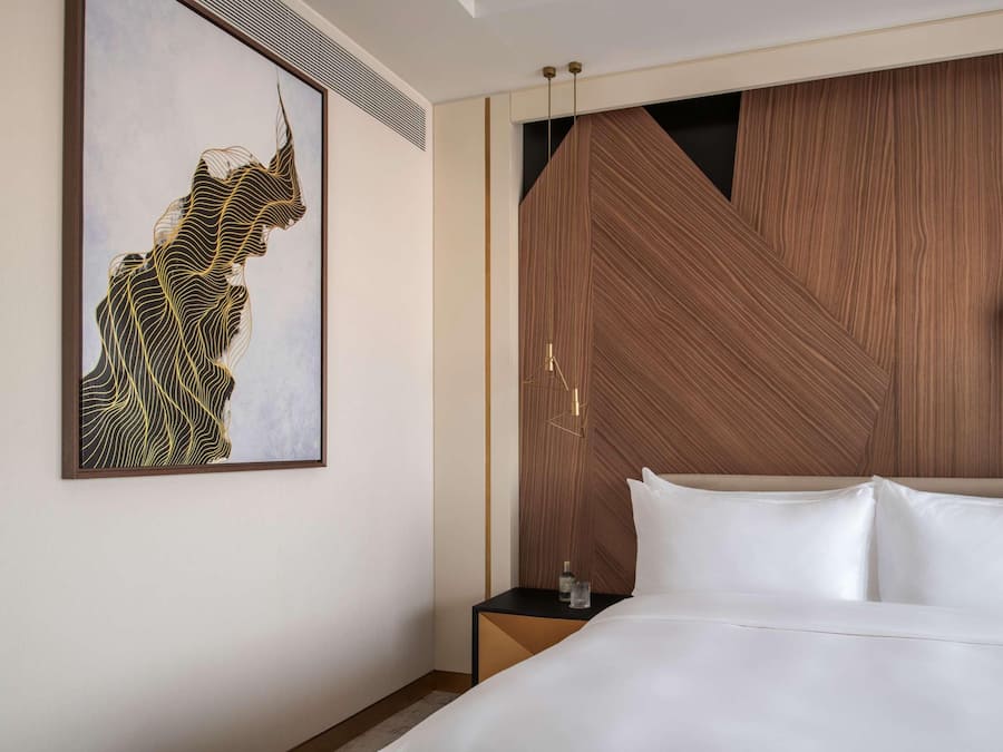 Ett modernt hotellrum med en stor säng, en väggpanel i trä och ett inramat konstverk på väggen.
