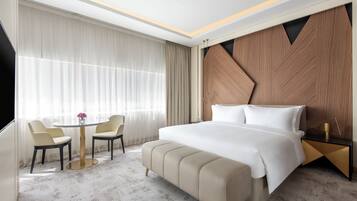 Habitación de hotel con una cama grande, una mesa redonda con sillas y vistas de la ciudad a través de amplias ventanas.