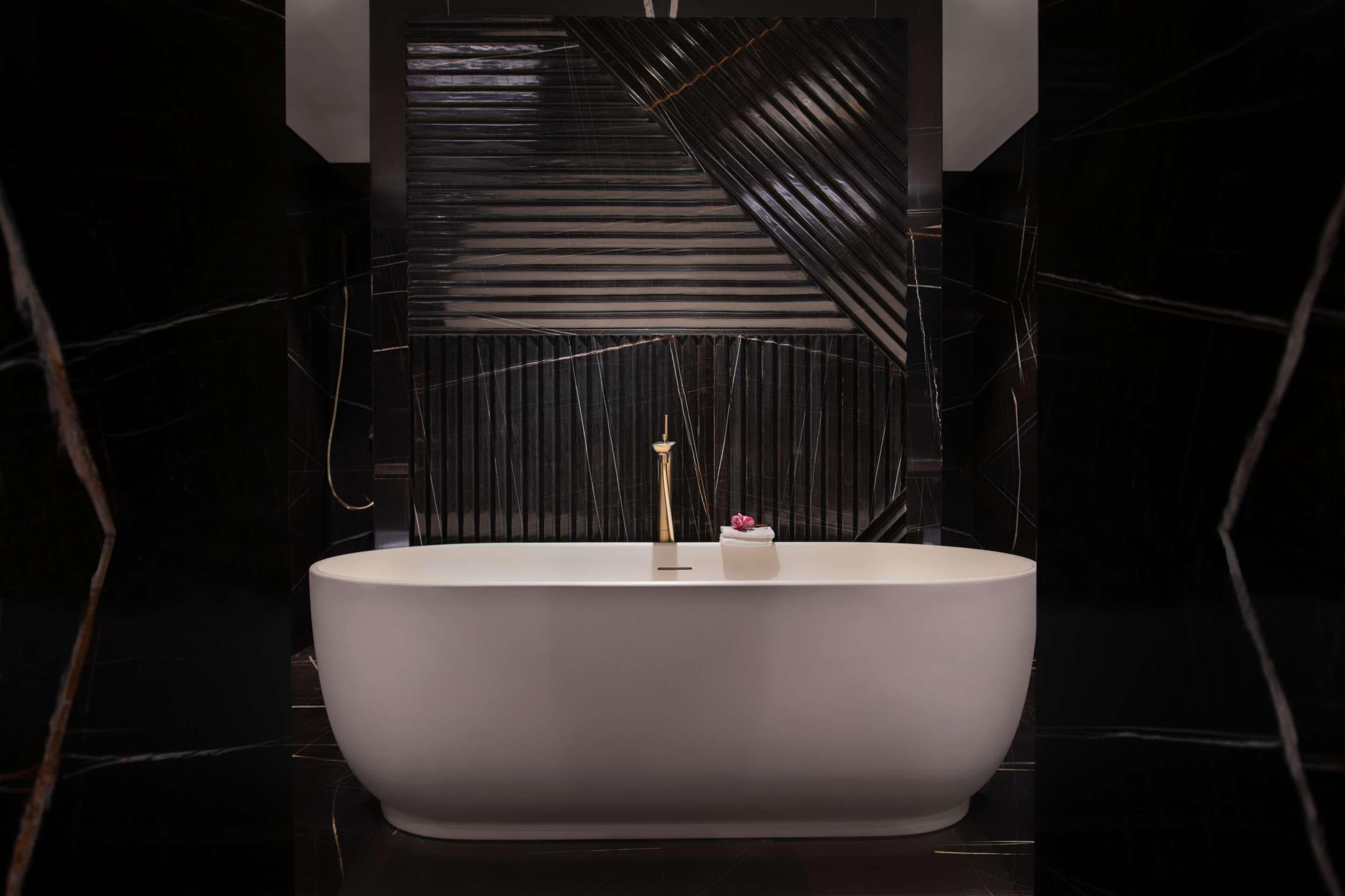 Un baño moderno con una bañera independiente, un grifo dorado y un pequeño objeto decorativo en el borde.