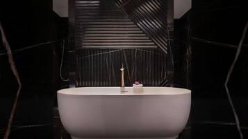 Un baño moderno con una bañera independiente, un grifo dorado y un pequeño objeto decorativo en el borde.