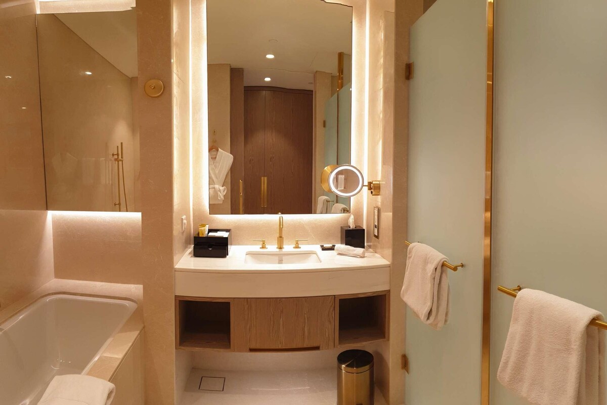 Ein modernes Badezimmer mit Badewanne, Waschbecken mit Waschtisch, Spiegel mit Beleuchtung und Handtuchhalter.