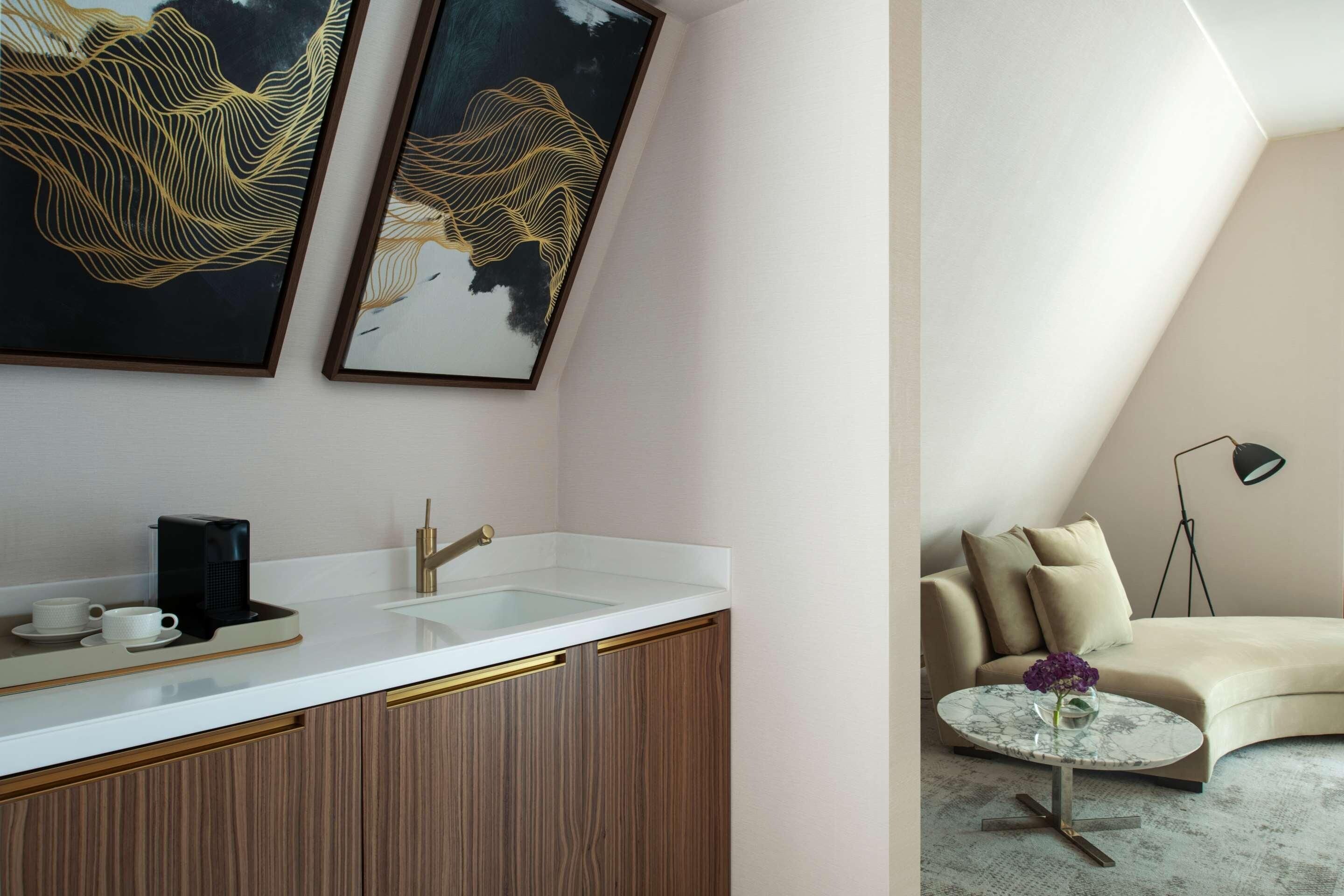 A modern kitchen with a white countertop, gold accents, and a coffee maker. There is a sink with a gold faucet, and two framed artworks above it.