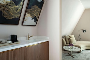 A modern kitchen with a white countertop, gold accents, and a coffee maker. There is a sink with a gold faucet, and two framed artworks above it.