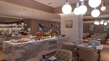 A modern hotel dining area with marble counters, round chandeliers, and neatly arranged tables.