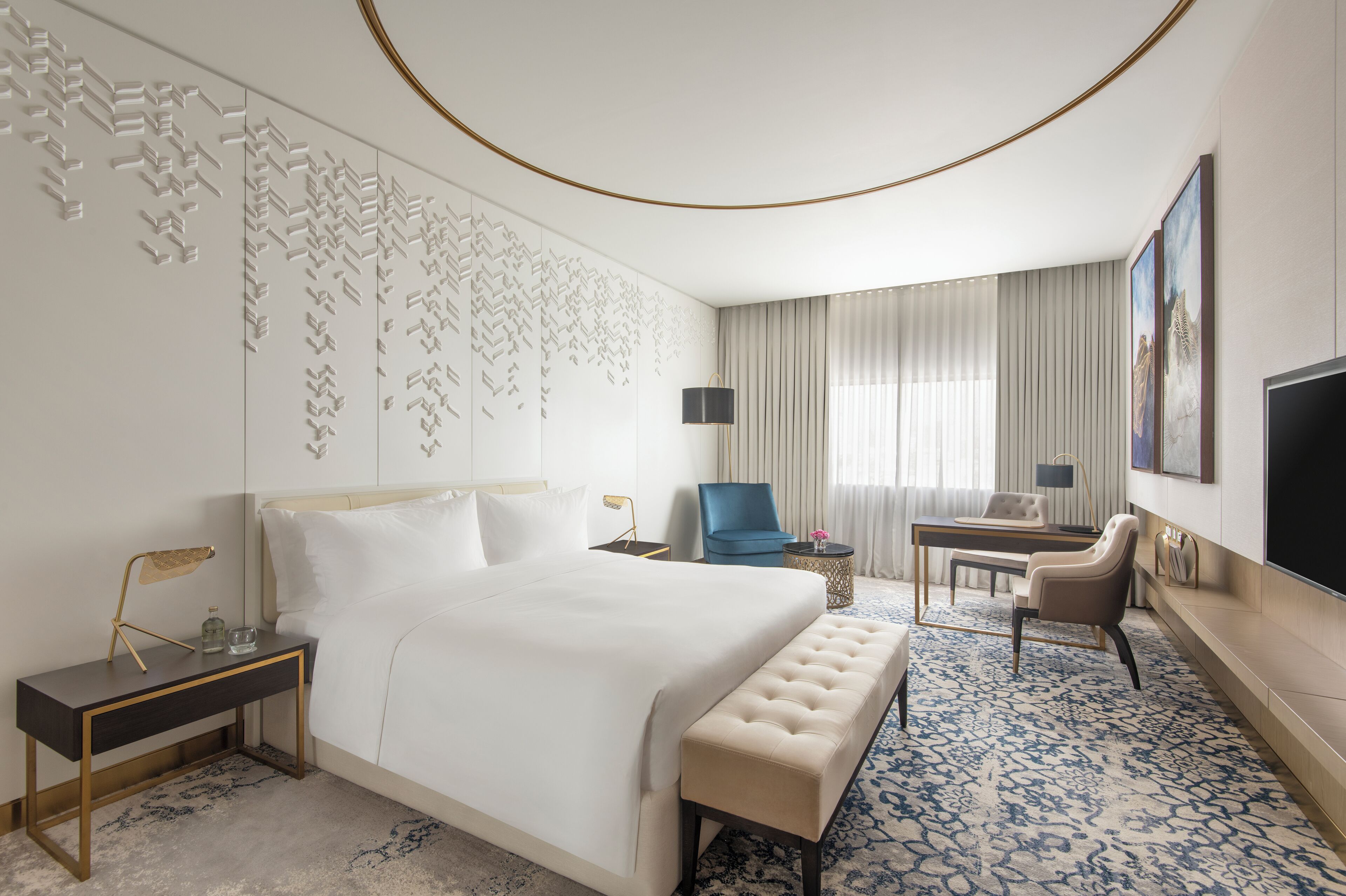 A hotel room with a large bed, a desk, a chair, a television, and a patterned carpet.