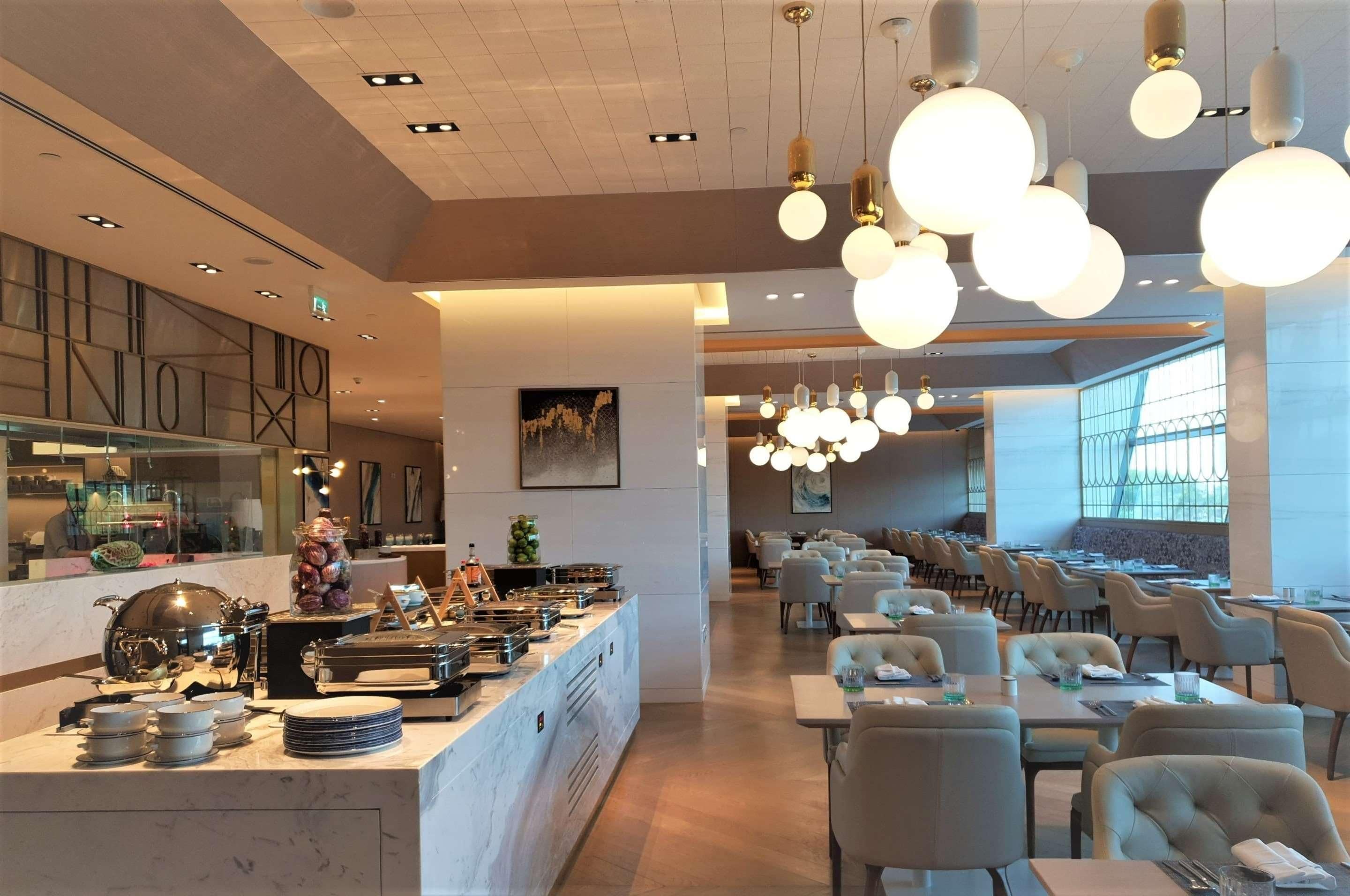 A modern restaurant with a buffet area, dining tables, and hanging spherical light fixtures.
