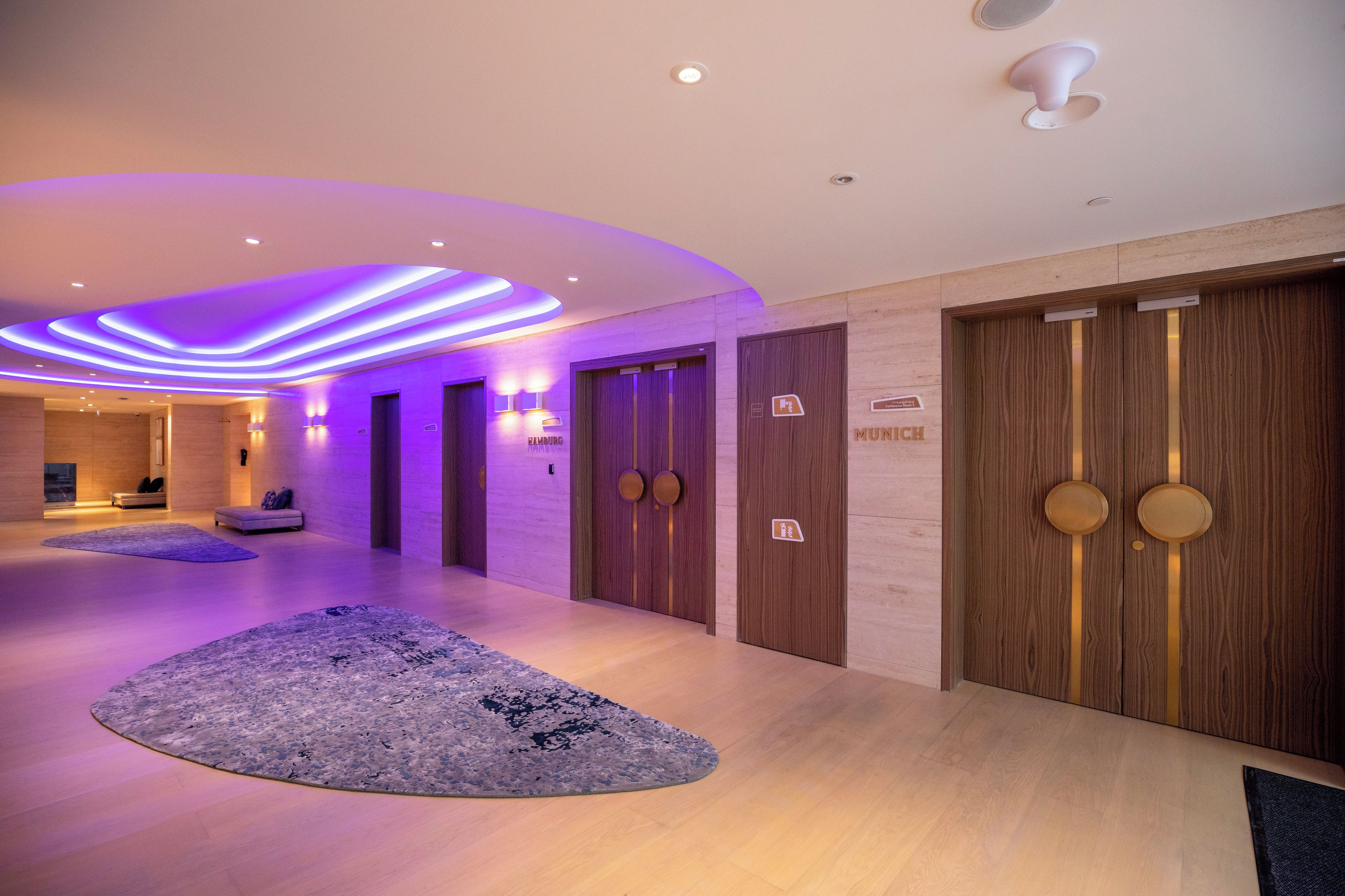 A modern hotel lobby with a wooden reception desk, a reception area, and a hallway leading to rooms.