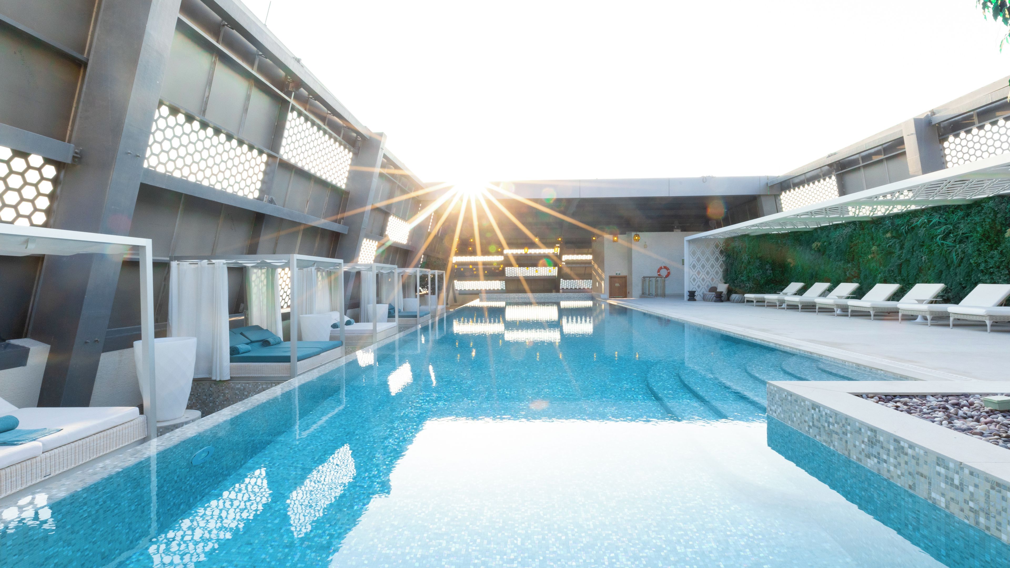 Una piscina interior moderna con áreas de descanso, techo de cristal y vistas al cielo.