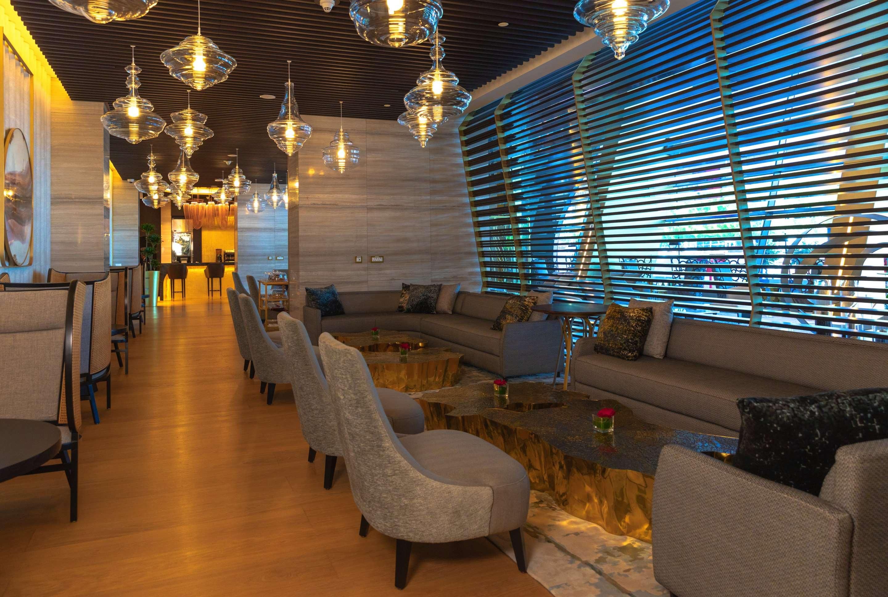 A modern lounge area with a long wooden bench, cushioned seating, and hanging pendant lights.