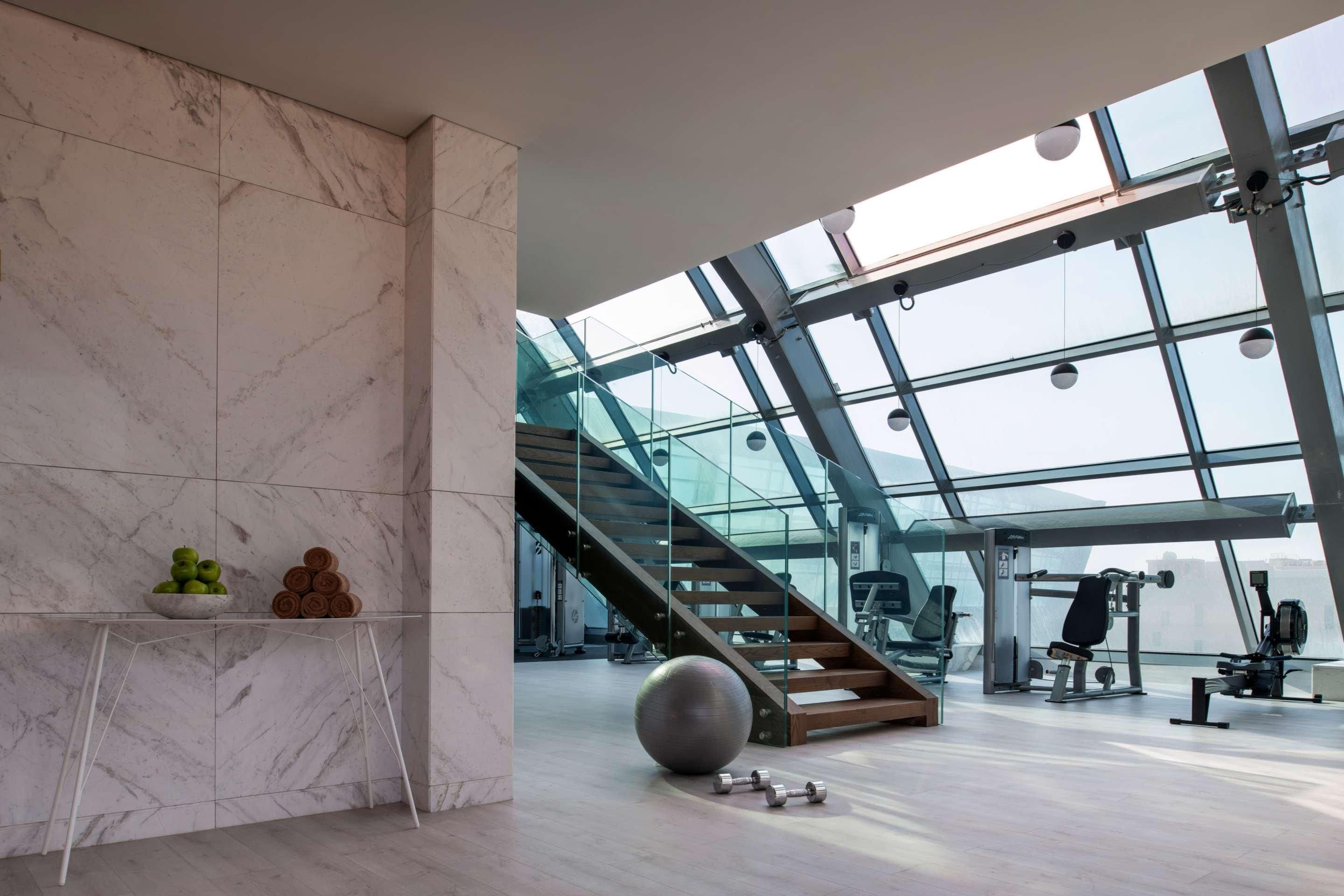 A modern gym with marble walls, a glass ceiling, and a staircase.