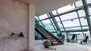 A modern gym with marble walls, a glass ceiling, and a staircase.