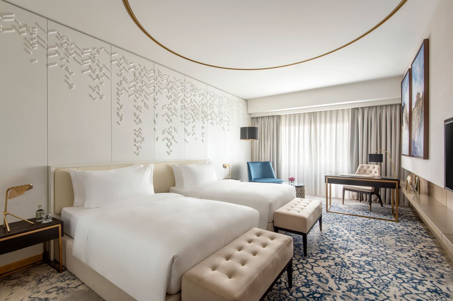 A hotel room with two beds, a desk, a chair, a small table, and a large window with curtains.
