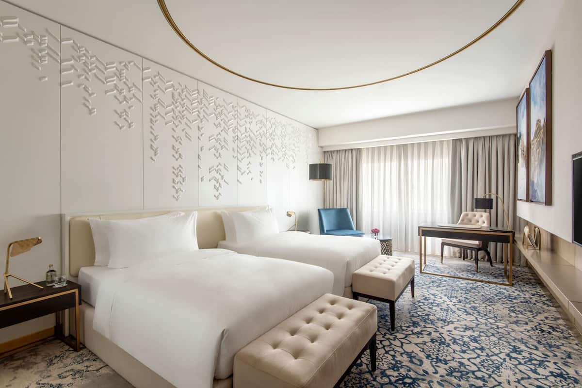 Habitación de hotel con dos camas, un escritorio, una silla, un televisor y un detalle decorativo en la pared.