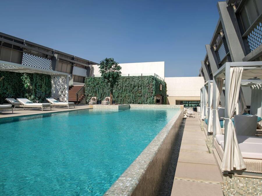 Une piscine entourée de chaises longues et de parasols, bordée d’un bâtiment moderne à la façade géométrique et agrémentée d’un mur végétal.