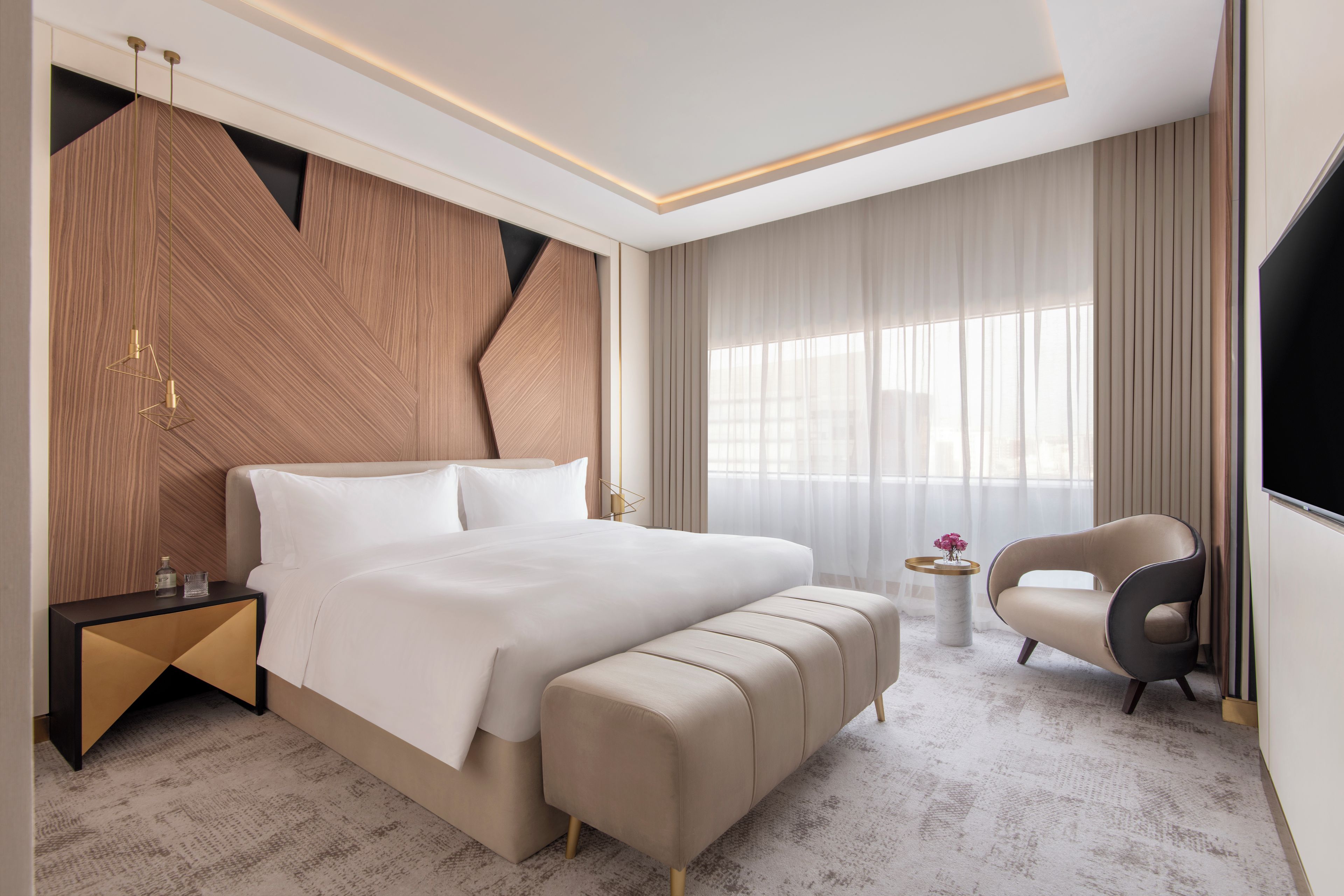 Una habitación de hotel moderna con una cama grande, una mesita de noche, una silla y un televisor.