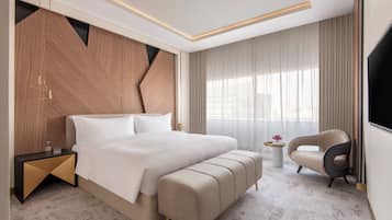 Una habitación de hotel moderna con una cama grande, una mesita de noche, una silla y un televisor.