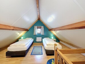 Un pequeño dormitorio en ático, con forma de triángulo, con dos camas individuales, una ventana con cortinas y techo de madera.