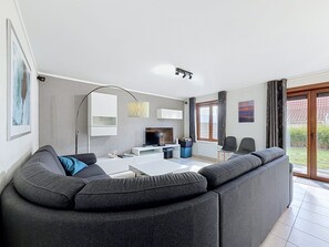 Een moderne woonkamer met een grijze modulaire bank, een flatscreen televisie en een eethoek met een witte tafel.