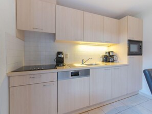 Una cocina moderna con alacenas de madera clara, lavavajillas integrado, cafetera y microondas.