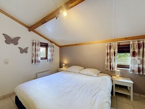 Un dormitorio con cama, dos mesitas de noche, una ventana con cortinas, una lámpara de pared y un ventilador de techo.
