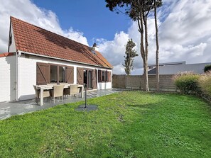 Una casa con techo de tejas, un patio con mobiliario exterior y un césped bien cuidado.