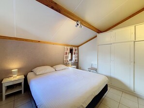 A bedroom with a bed, nightstands, a wardrobe, and a window with curtains. - Vissershuisje Nova with parking by Interhome (De Haan)