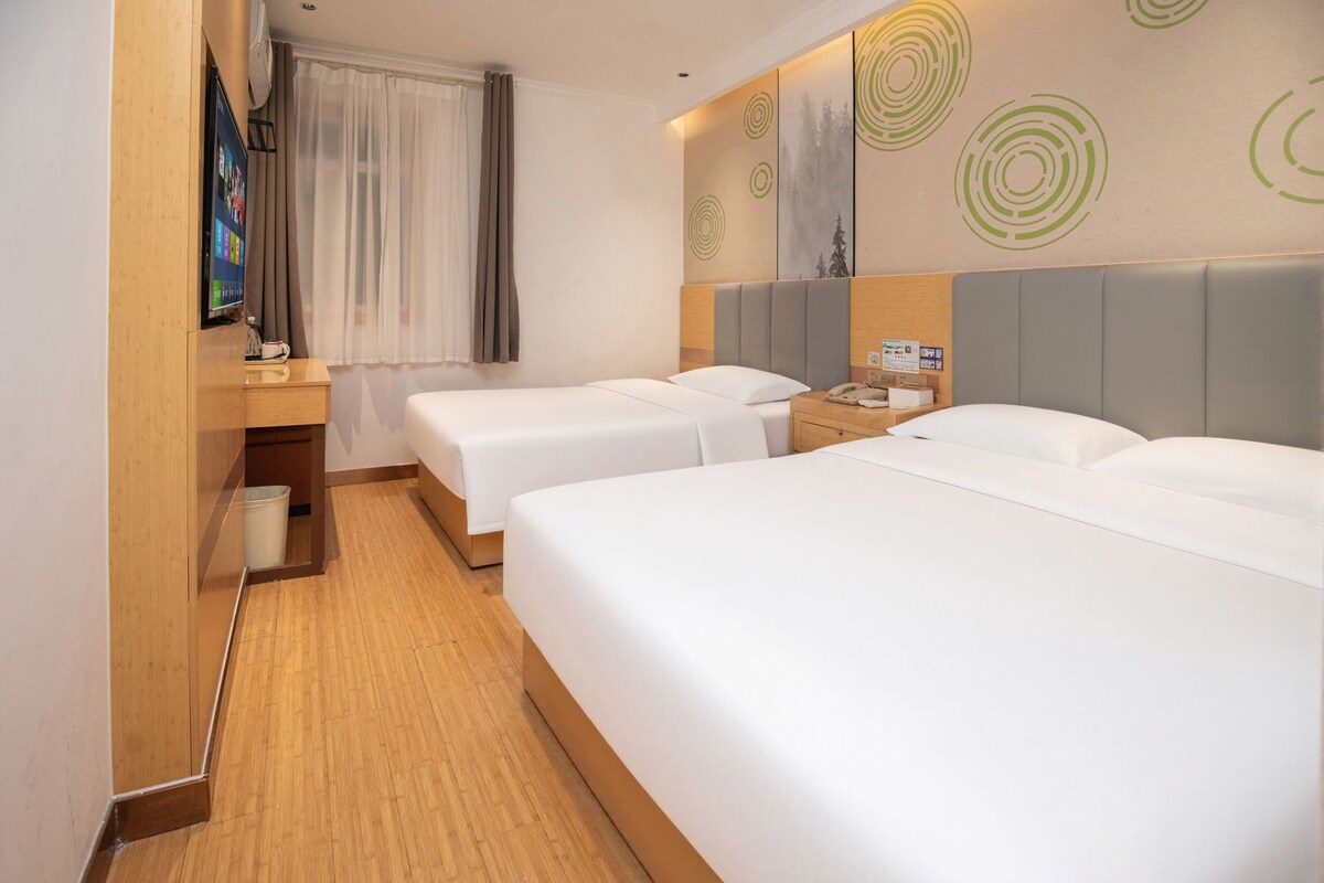 Ein Hotelzimmer mit zwei Betten, einem Holztisch, einem Fernseher und einem Fenster mit Vorhängen.