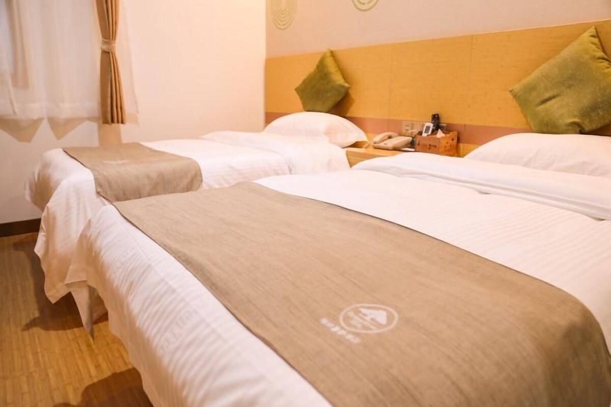 Une chambre d’hôtel avec deux lits, une tête de lit en bois, une table de chevet avec un téléphone et une fenêtre avec des rideaux.