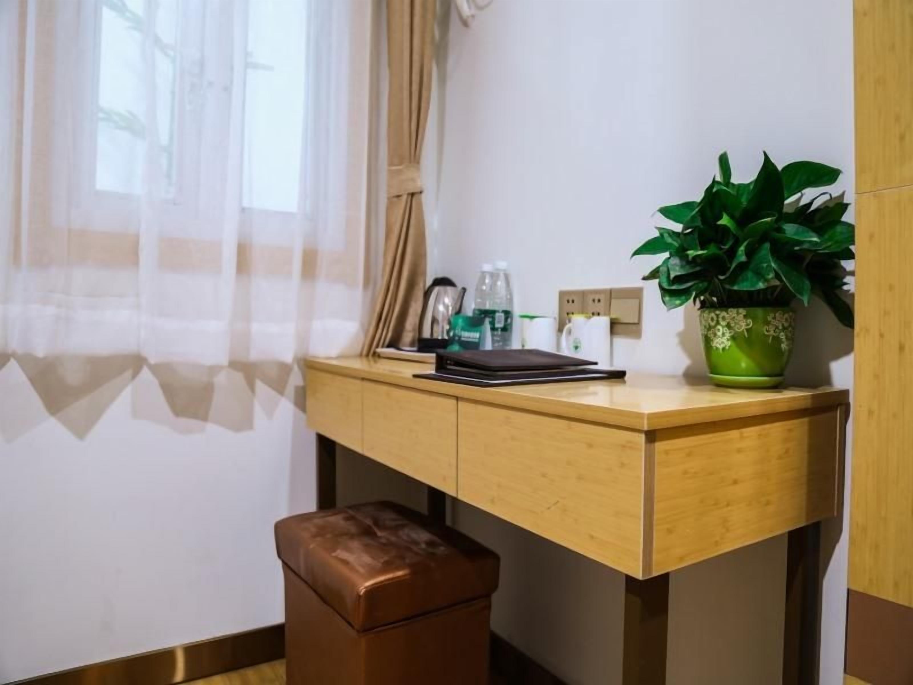 A wooden desk with a laptop, a green plant, and a brown leather stool.