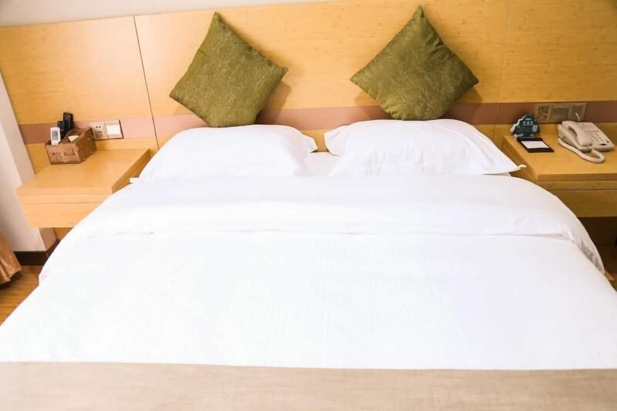 Ein Hotelzimmer mit einem großen Bett, zwei grünen Kissen, weißer Bettwäsche, einem Holz-Kopfteil, einem Nachttisch mit Telefon und Taschentuchbox.