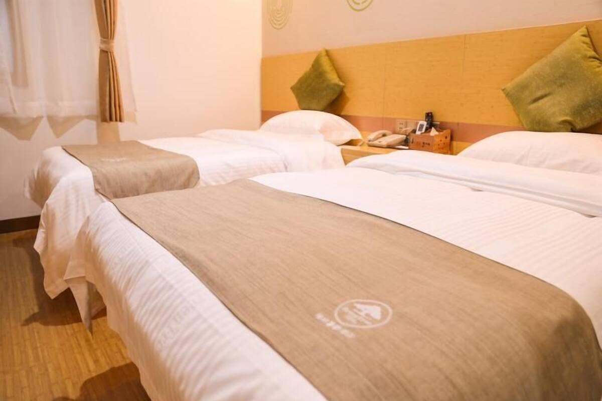 Ein Hotelzimmer mit zwei Betten, einem Holzkopfende, einem Nachttisch mit Telefon und einem Fenster mit Vorhängen.