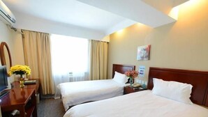 A hotel room with two beds, a desk with a computer, a vase with flowers, and a window with curtains. - Greentree Inn Nanjing Zhongshan Mausoleum Scenic Area Zhongling Street Subway Station Express Hotel (Nanjing)