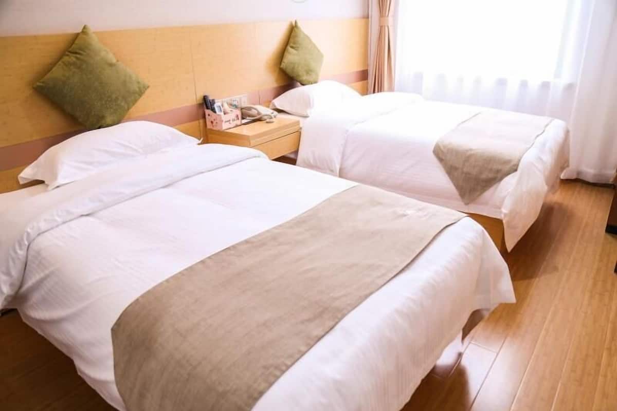Ein Hotelzimmer mit zwei Betten, Holzboden und einem Nachttisch mit Lampe und kleinem Tisch.