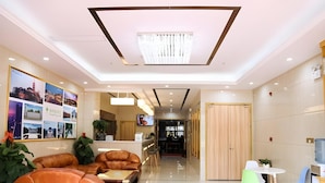 A hotel lobby with a reception desk, seating area with sofas, a dining table with chairs, and a large wall with framed pictures. - Greentree Inn Nanjing Zhongshan Mausoleum Scenic Area Zhongling Street Subway Station Express Hotel (Nanjing)